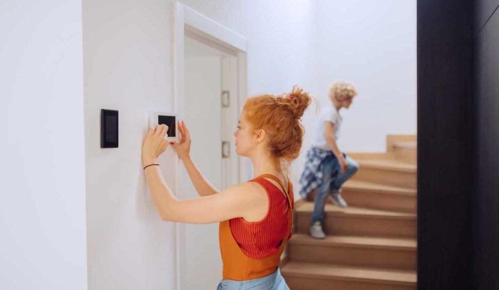 Nuori nainen säätää talon älytoimintoja pieneltä seinänäytöltä