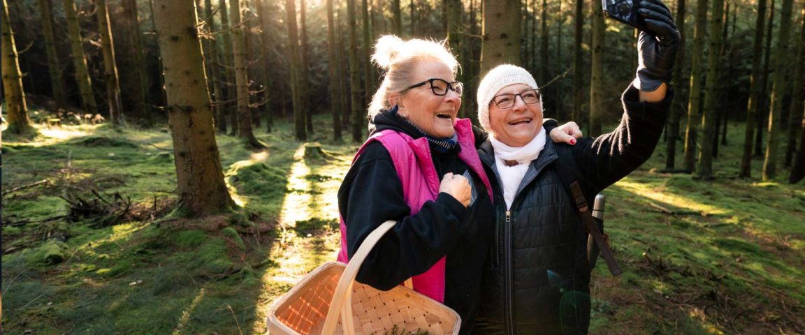 Two ladies in a forest searching for mushrooms